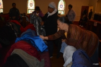 A church member, foreground, sorts the coats as a guest examines one.